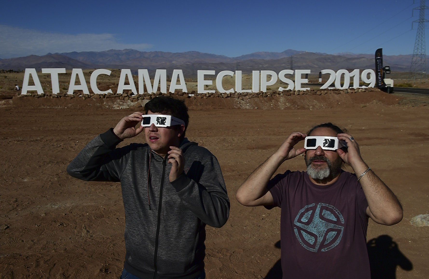 Turistas prueban gafas especiales para ver un eclipse en la entrada de un campamento astronómico en la comuna de Vallenar en el desierto de Atacama. (Foto: AFP)